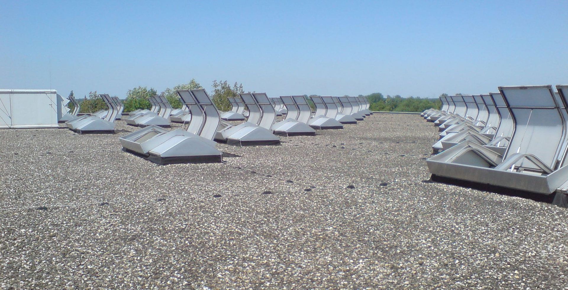 Flachdach eines Industriegebäudes mit zahlreichen aufgereihten Lichtband-Oberlichtern aus Aluminium, die in zwei parallelen Reihen angeordnet sind